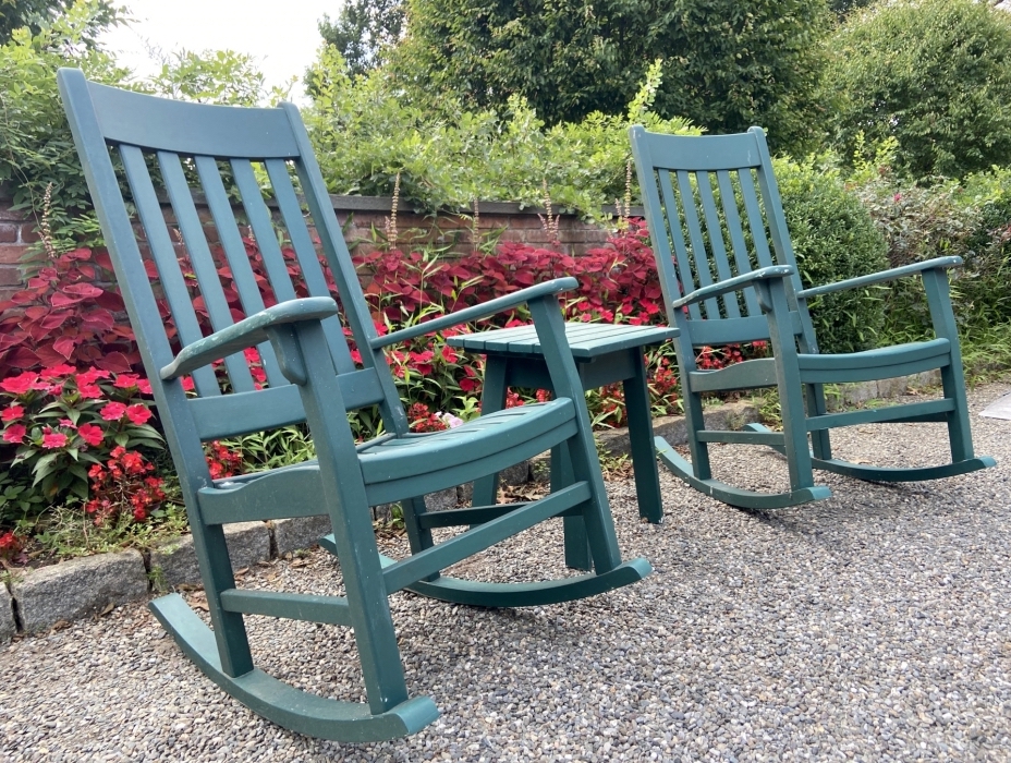 A pair of wooden green-painted outdoor rocking chairs flank a compatible table perfect for cocktails or a great summer read.